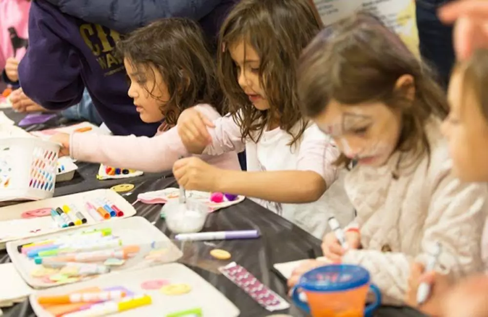 Several children work side by side at a table with arts supplies.