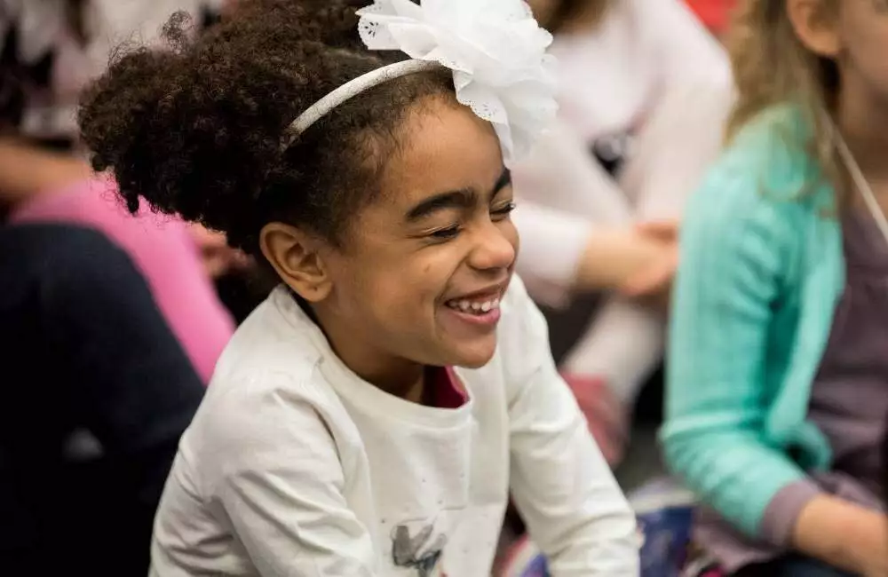 A young student sitting amongst her classmates giggles.