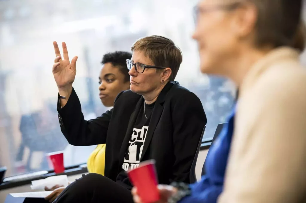 A school leader sitting amongst a group raises her hand.