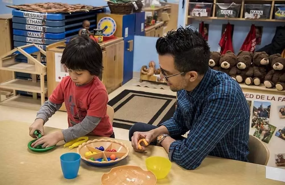 A teacher watches as a young child works with colorful learning tools.